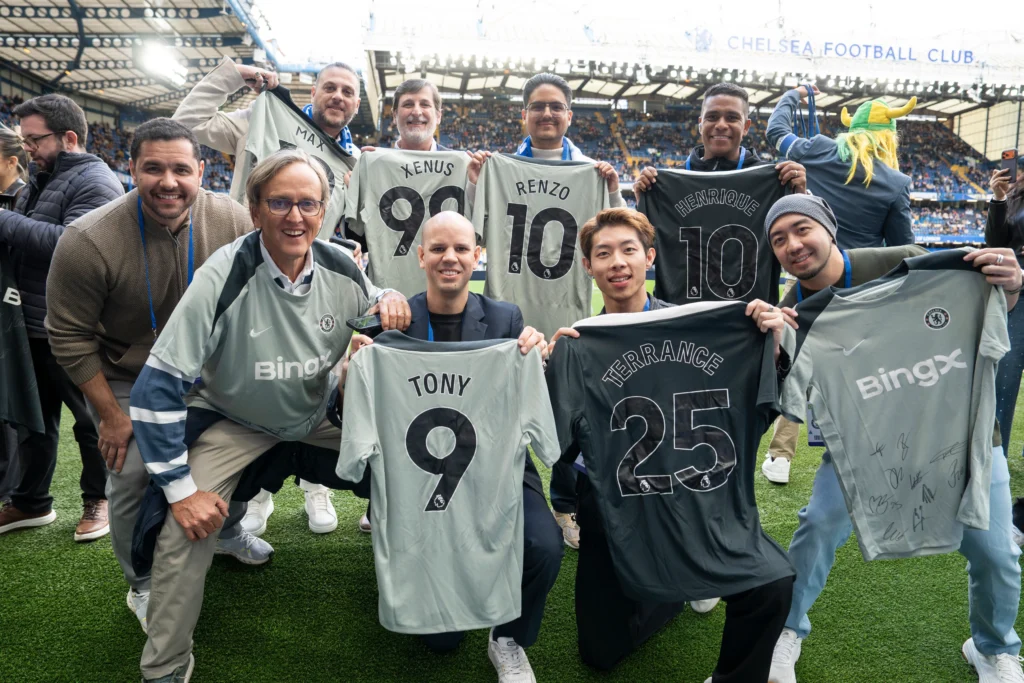 BingX VIPs holding personalised signed Chelsea FC jerseys on Stamford Bridge pitch